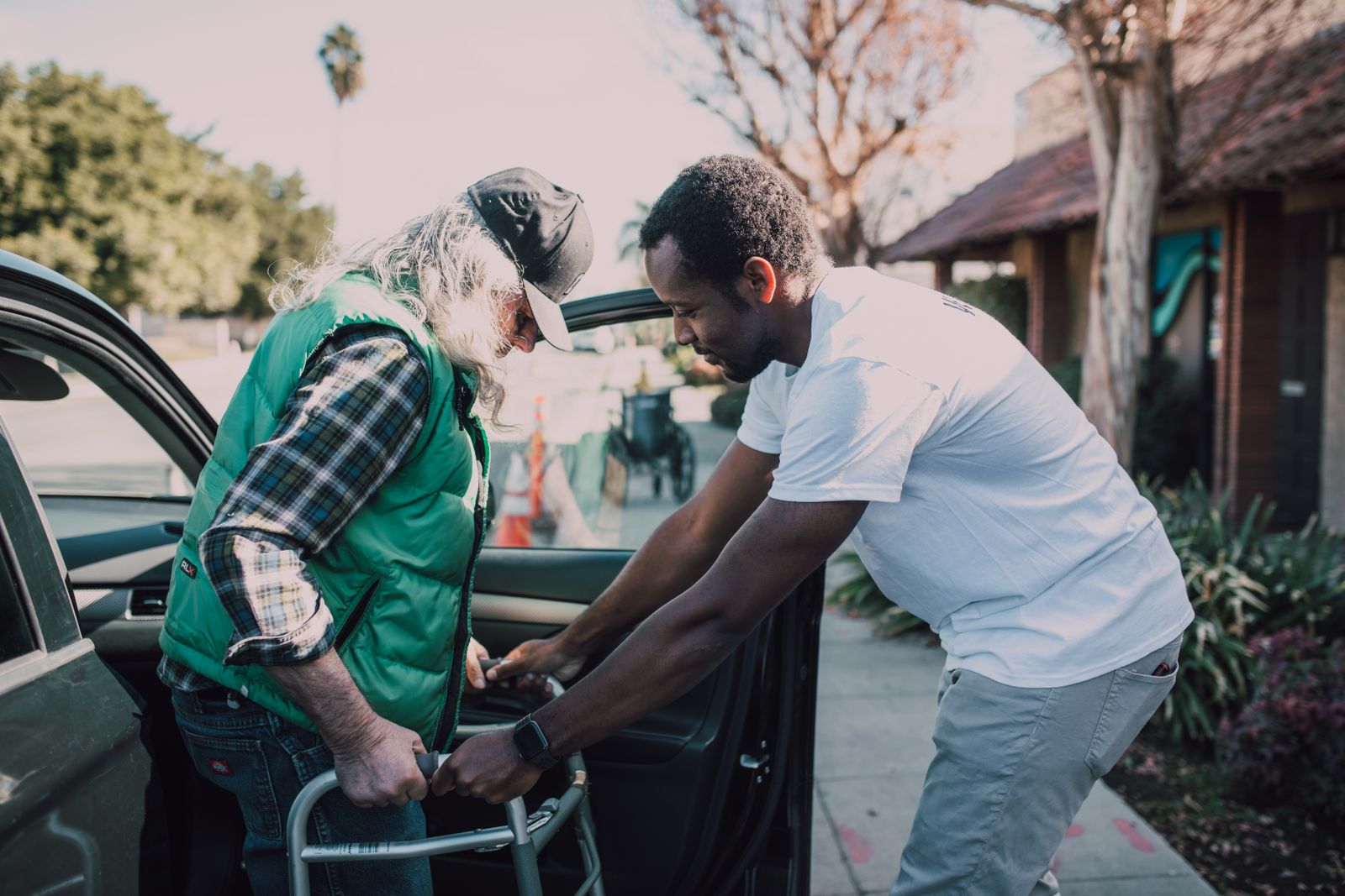 A caregiver helping an older man with a walker get into a car
