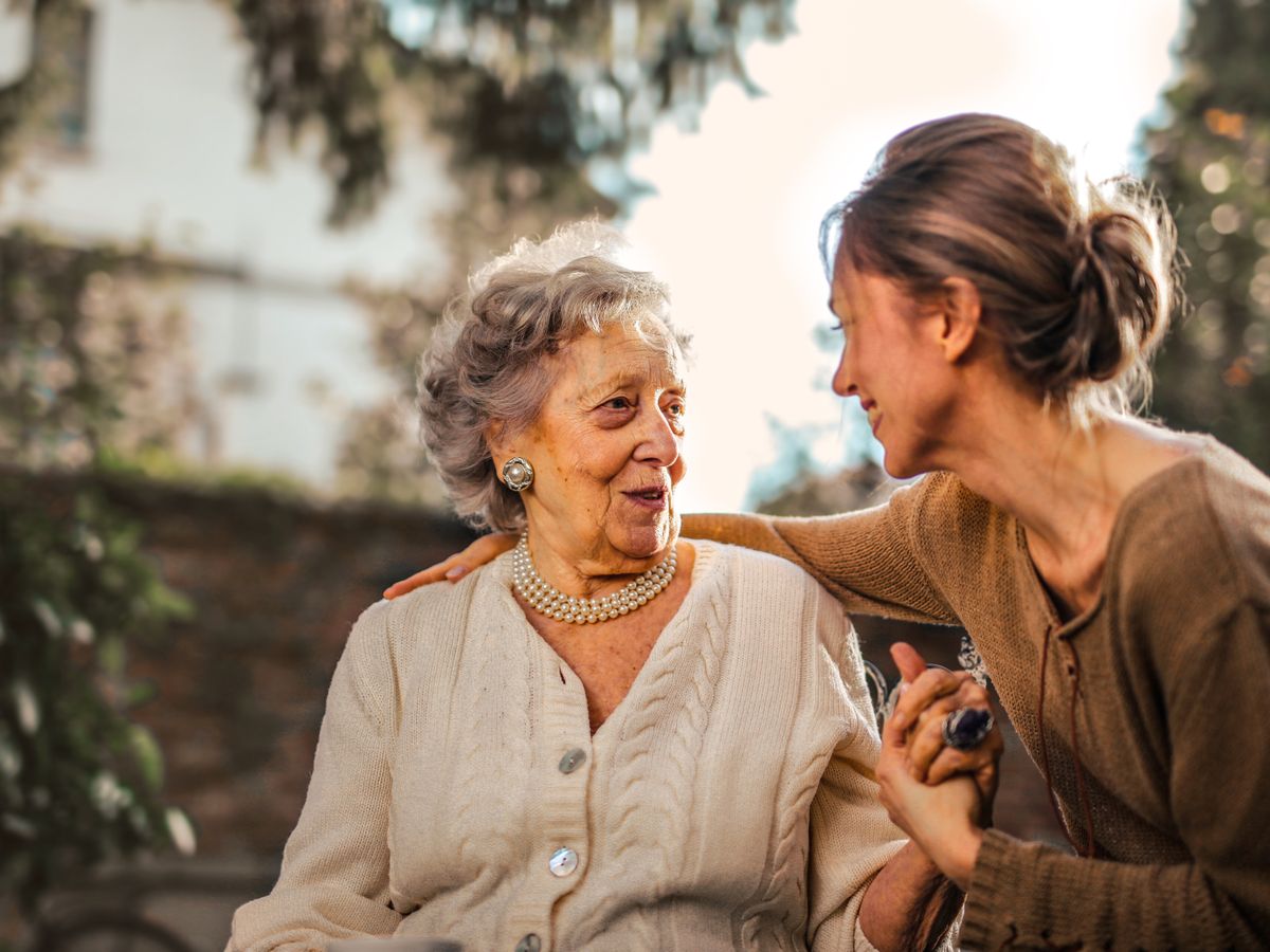 A caregiver and an older woman talking and laughing together outdoors