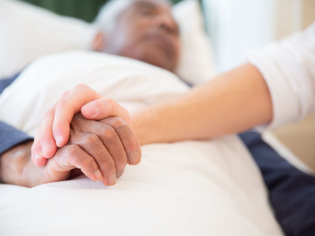 A caregiver holding the hand of an older man resting in bed